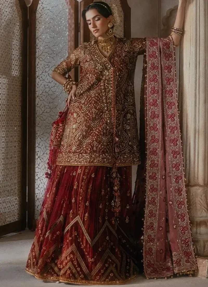 Full-length front view of a brick red peplum shirt with gharara, ornate gold embroidery, embellished neckline, geometric gharara border and pink embroidered dupatta.
