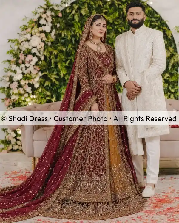 Real Shadi Dress bride wearing a heavily embroidered maroon Pakistani bridal dress with her groom at the wedding.
