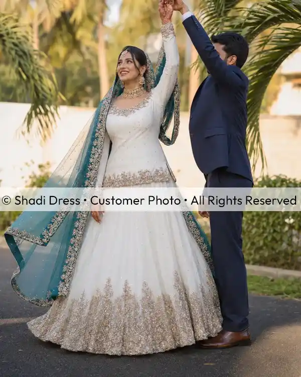 Real Shadi Dress bride wearing a white embroidered Pakistani bridal dress with a teal dupatta beside her groom.
