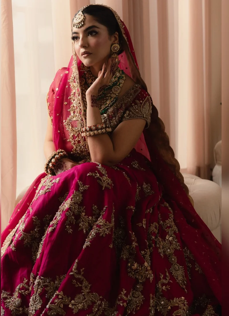 Raspberry pink bridal lehenga choli with intricate gold dabka and tilla embroidery, cascading floral arch motifs, ornate hem border and sheer pink dupatta.