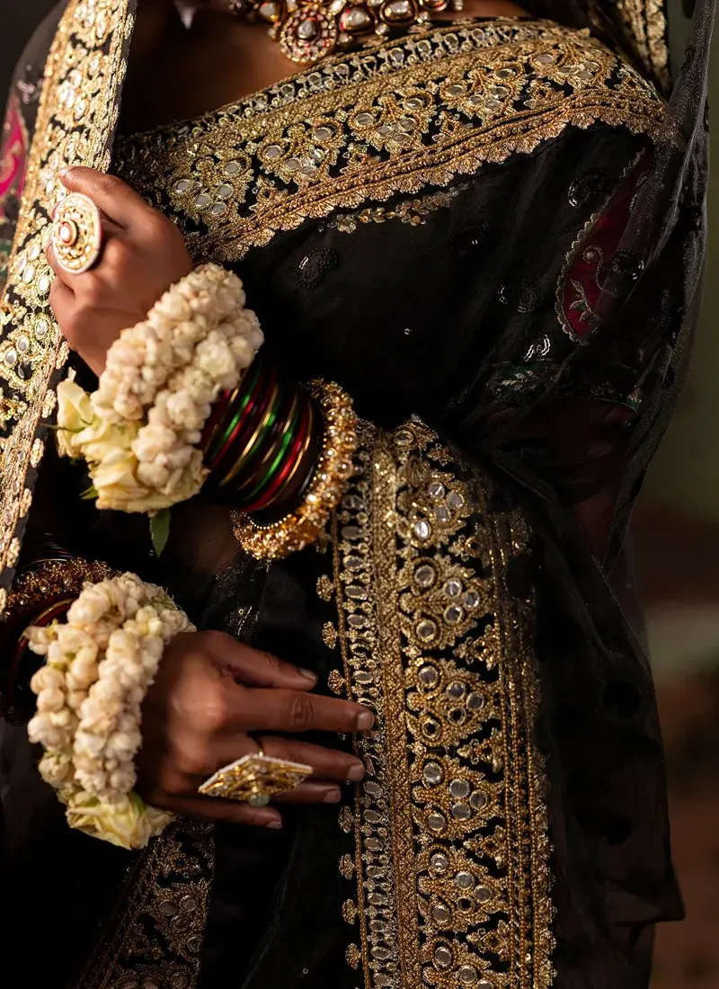 Black bridal saree, full front view, with sweeping gold panni border and ornate floral hem.