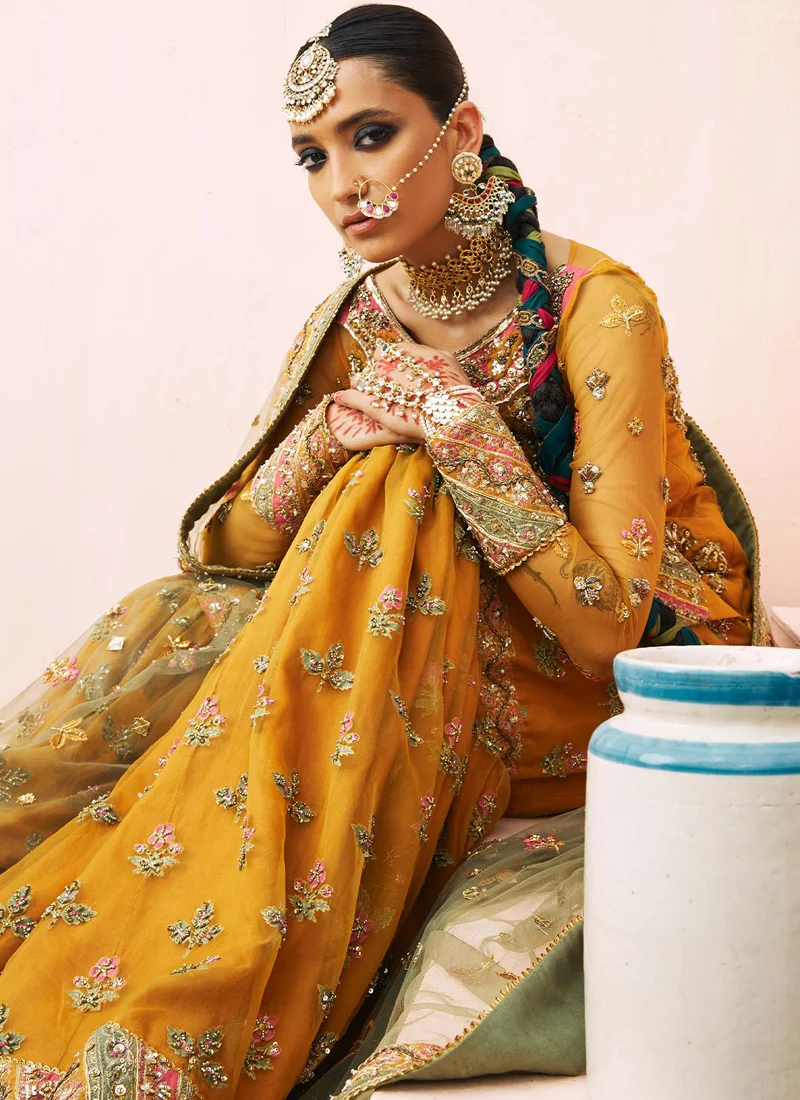 Mustard gharara suit seated wide view with voluminous flared legs, diagonal embellished hems and olive net dupatta