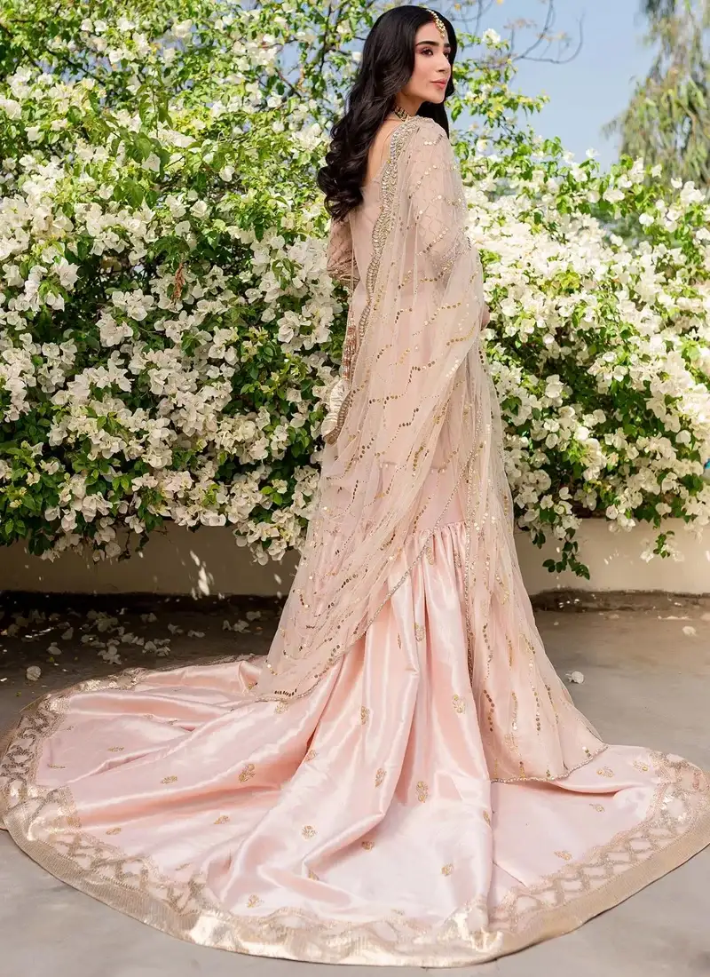 Peach farshi gharara with sheer net dupatta draped over the head and a wide gold-bordered trailing hem