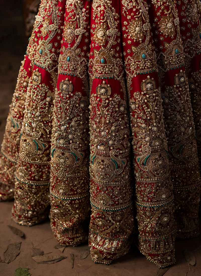 Red bridal lehenga choli seated view with sheer red dupatta and pearl embellished gold skirt borders